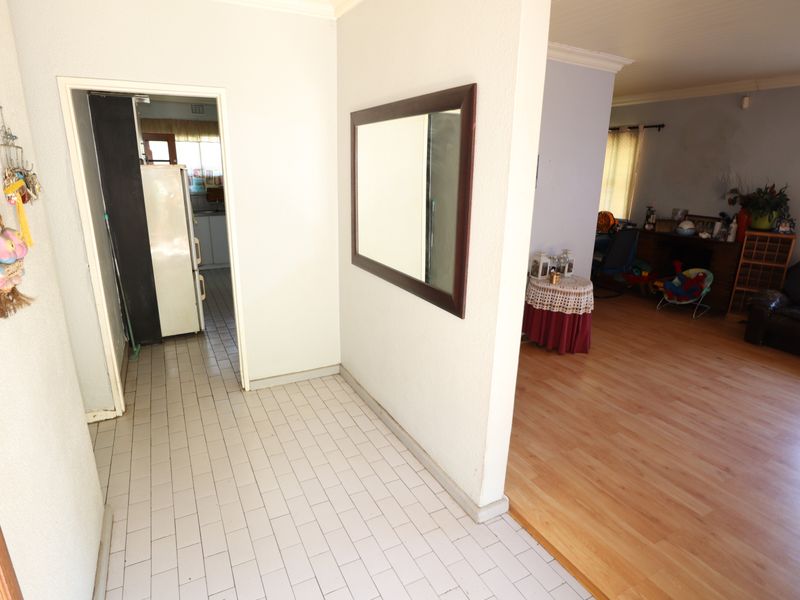 A functional hallway area featuring tiled flooring, connecting to the living room with laminate flooring and providing access to the kitchen.