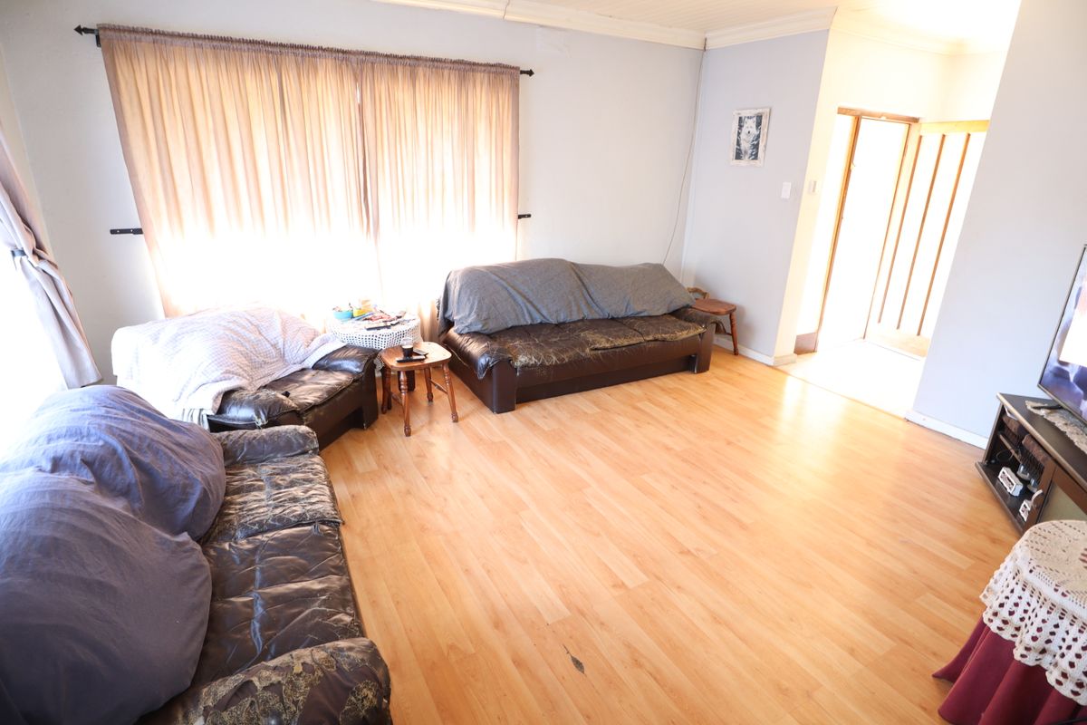 A living room featuring laminate flooring and coved ceilings, offering a functional space with potential for cosmetic updates.