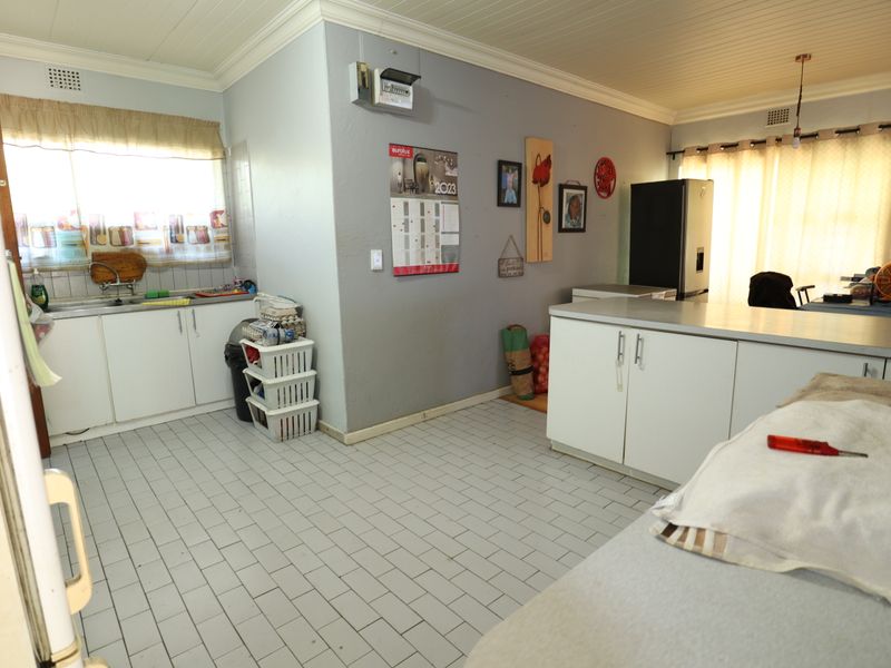Functional kitchen featuring white built-in cabinetry, laminate countertops, a stainless steel sink, and tiled flooring with a classic tongue and groove ceiling.