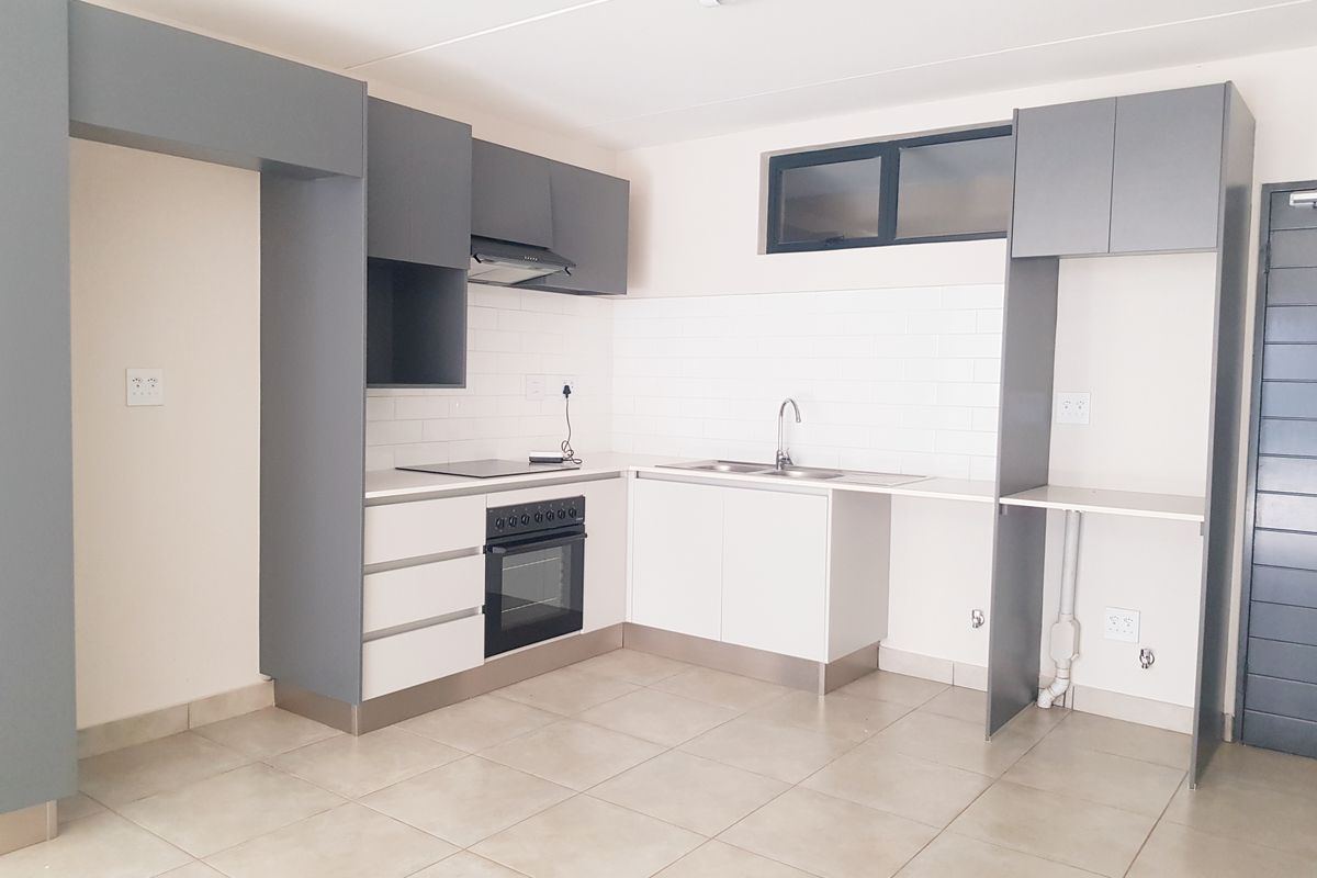 Modern kitchen featuring grey and white cabinetry, built-in oven and hob, subway tile backsplash, and tiled flooring in a clean, empty space.