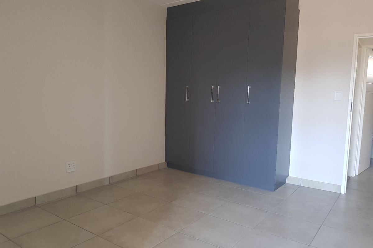 A clean, empty bedroom featuring neutral tiled flooring and modern dark grey built-in cupboards, providing a blank canvas for personalization.