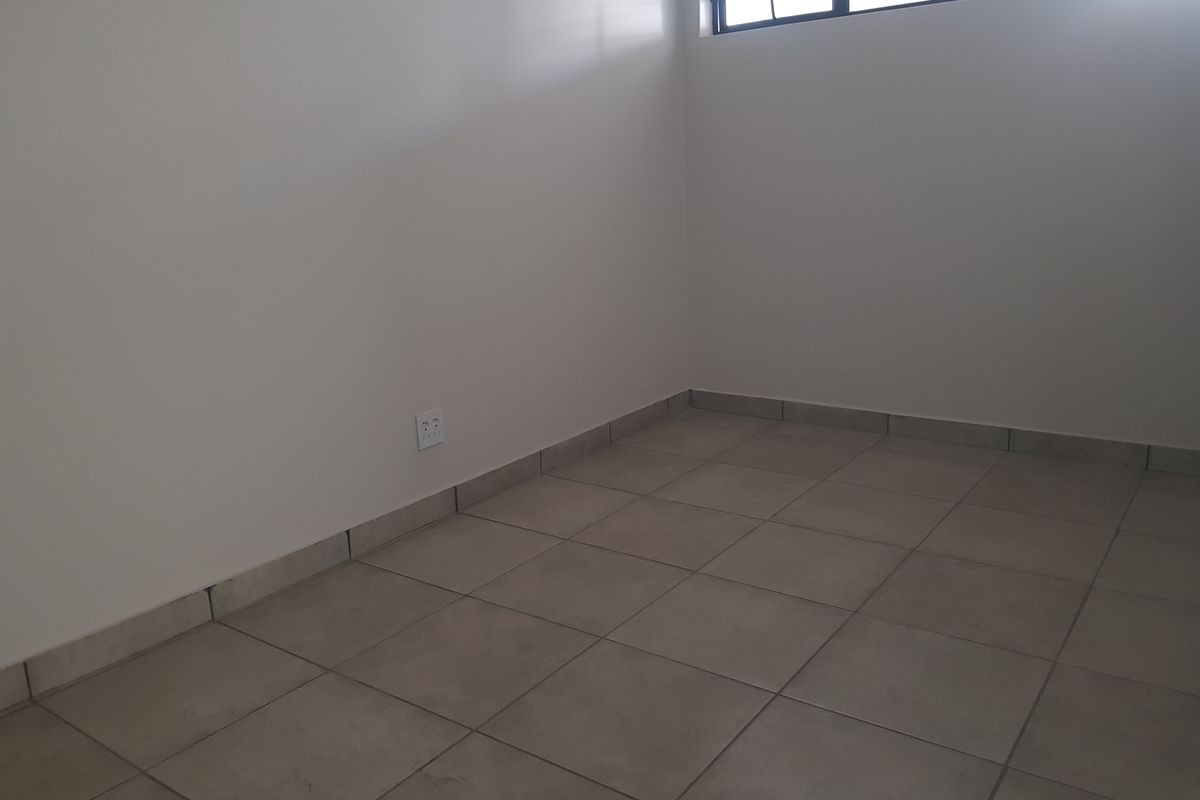 An empty bedroom featuring neutral tiled flooring and a high-set window, providing a blank canvas for personalization.