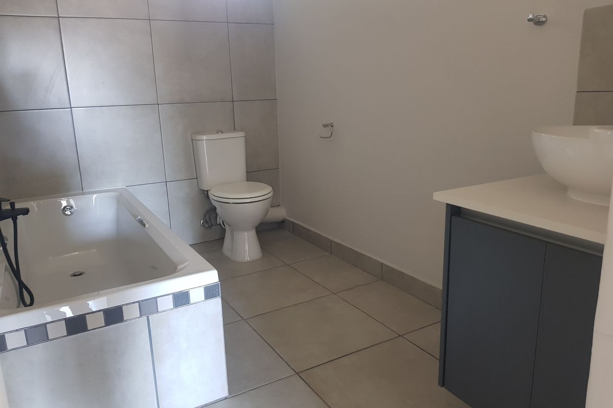 A modern bathroom featuring a built-in bathtub, a white ceramic toilet, and a vanity cabinet with a vessel sink.