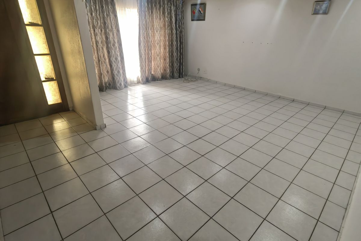 A spacious, empty living room featuring neutral ceramic floor tiles, a timber ceiling, and a glass-panelled entrance door.