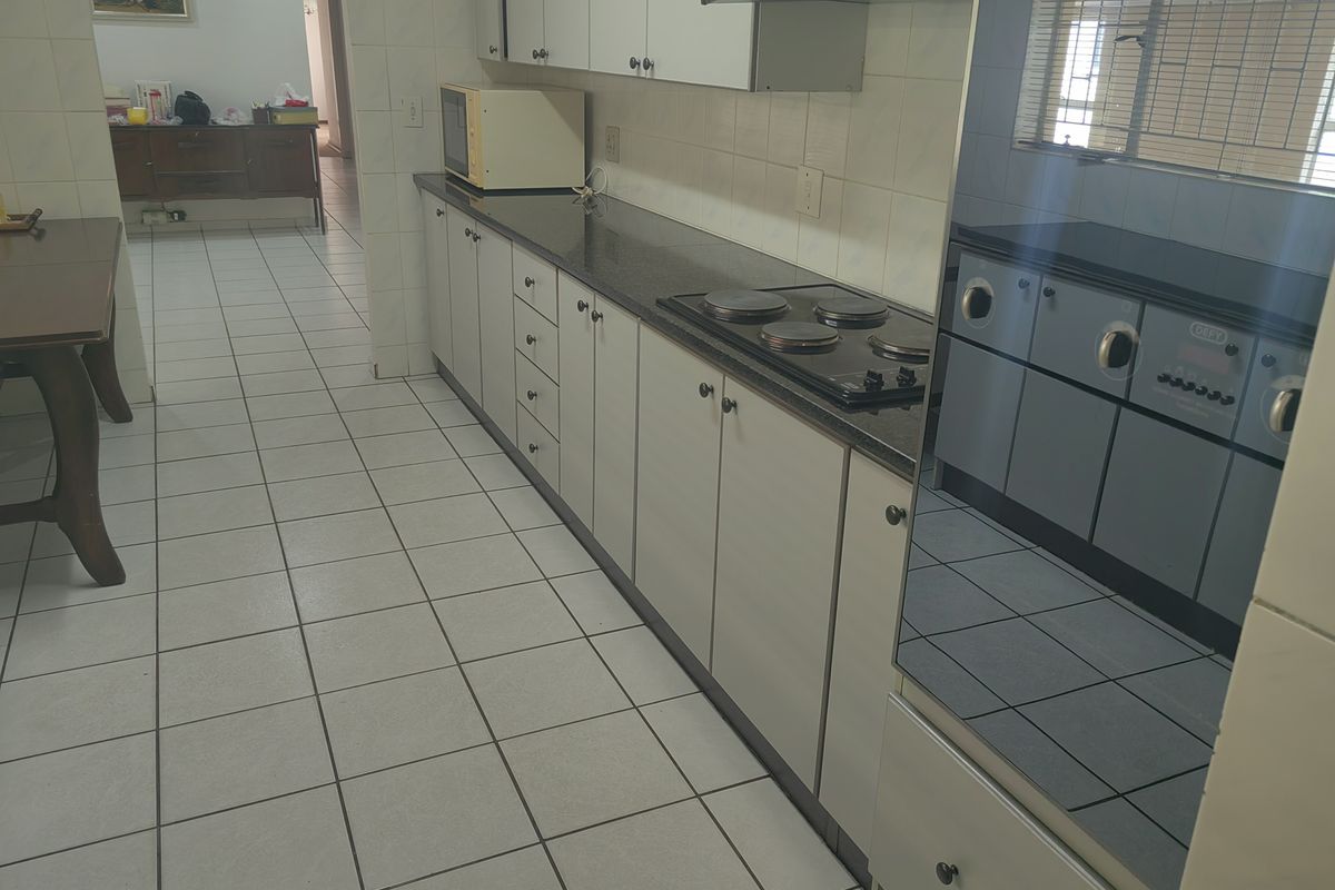 A functional kitchen featuring built-in cabinetry, granite countertops, an integrated electric hob, and an oven, with tiled flooring throughout.