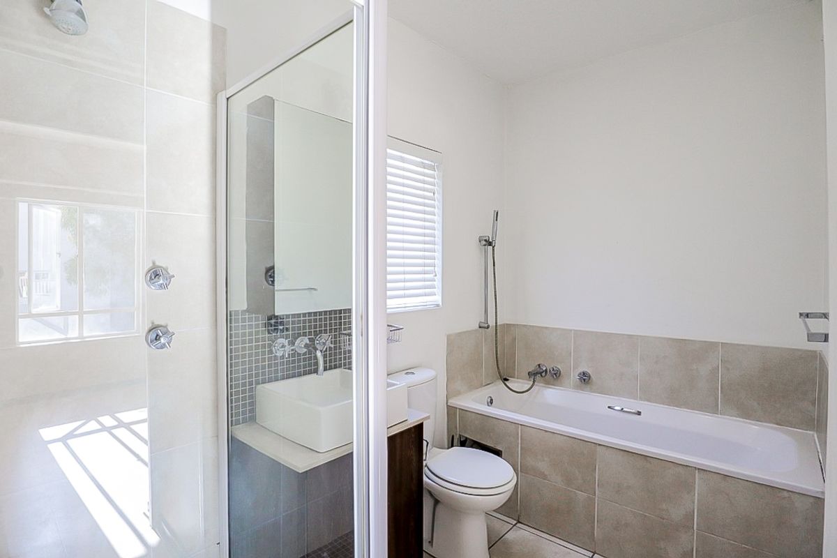A modern bathroom featuring a tiled bathtub, a separate glass-enclosed shower, a vanity with a basin, and a toilet.