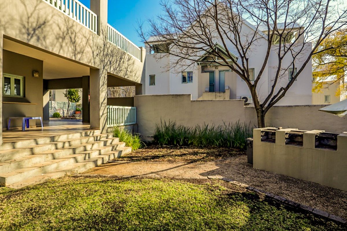 Rear exterior view featuring a covered patio area, concrete stairs, a built-in brick braai, and a small garden space.