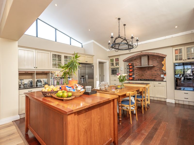 Spacious kitchen featuring a brick feature wall, vaulted ceilings with clerestory windows, hardwood flooring, and extensive built-in cabinetry with integrated appliances.
