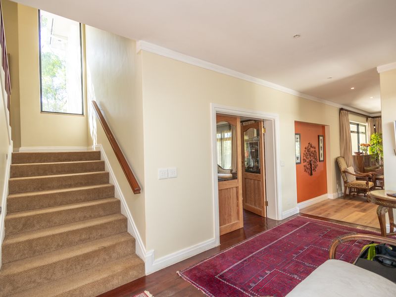 Welcoming entrance hall featuring a carpeted staircase with a timber handrail, hardwood flooring, and access to adjacent living spaces through a classic wooden door.