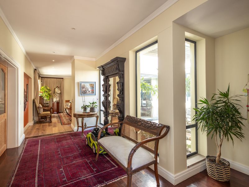 A spacious, well-lit hallway featuring polished hardwood flooring, decorative cornice detailing, and large windows that provide a view into the adjacent courtyard area.