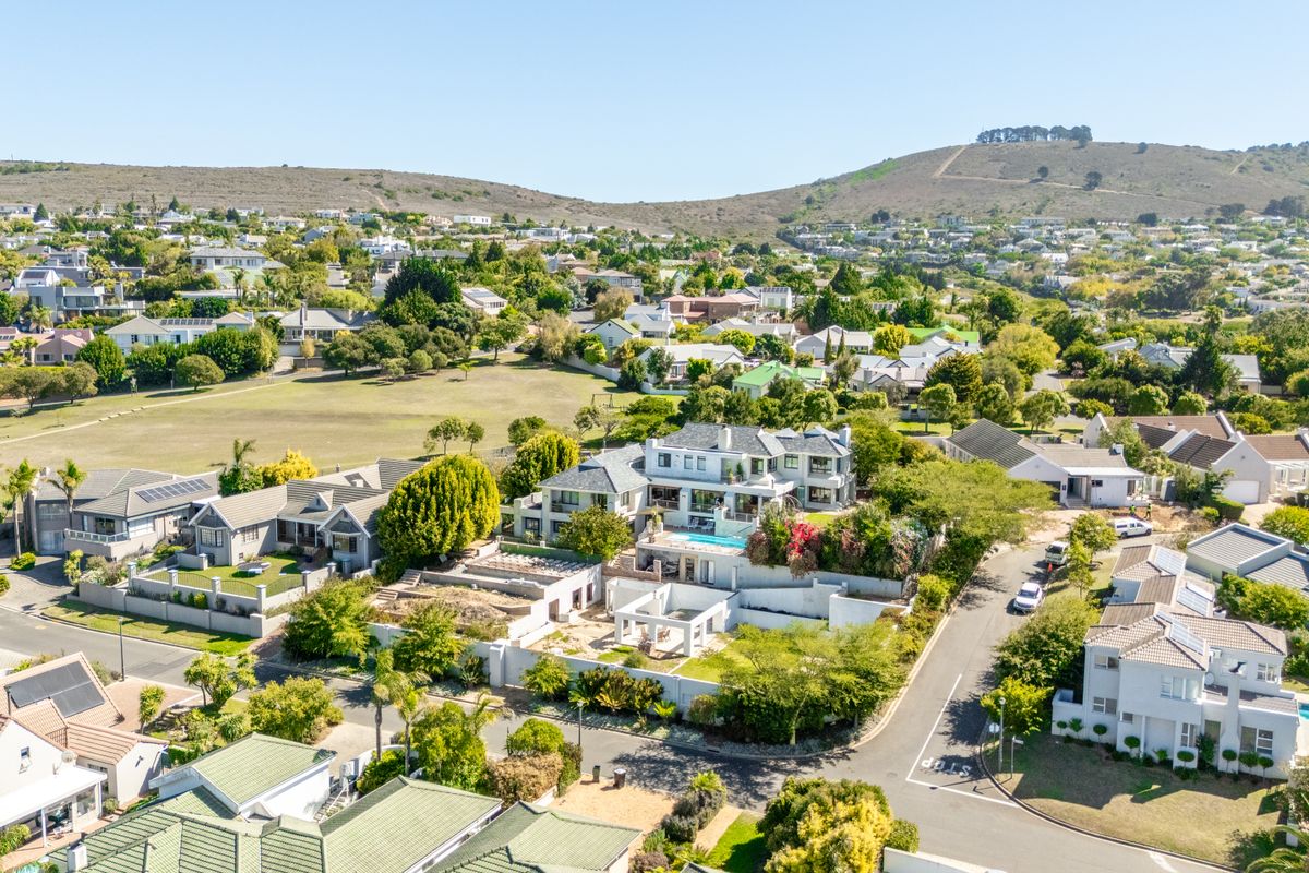 An aerial view of a residential estate featuring multiple homes, landscaped gardens, swimming pools, and surrounding neighborhood infrastructure.