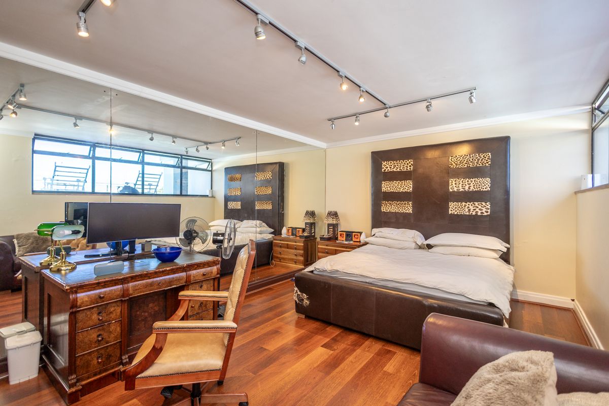 Spacious bedroom featuring polished hardwood flooring, extensive wall-to-wall mirrors, and modern track lighting, creating a bright and functional living space.
