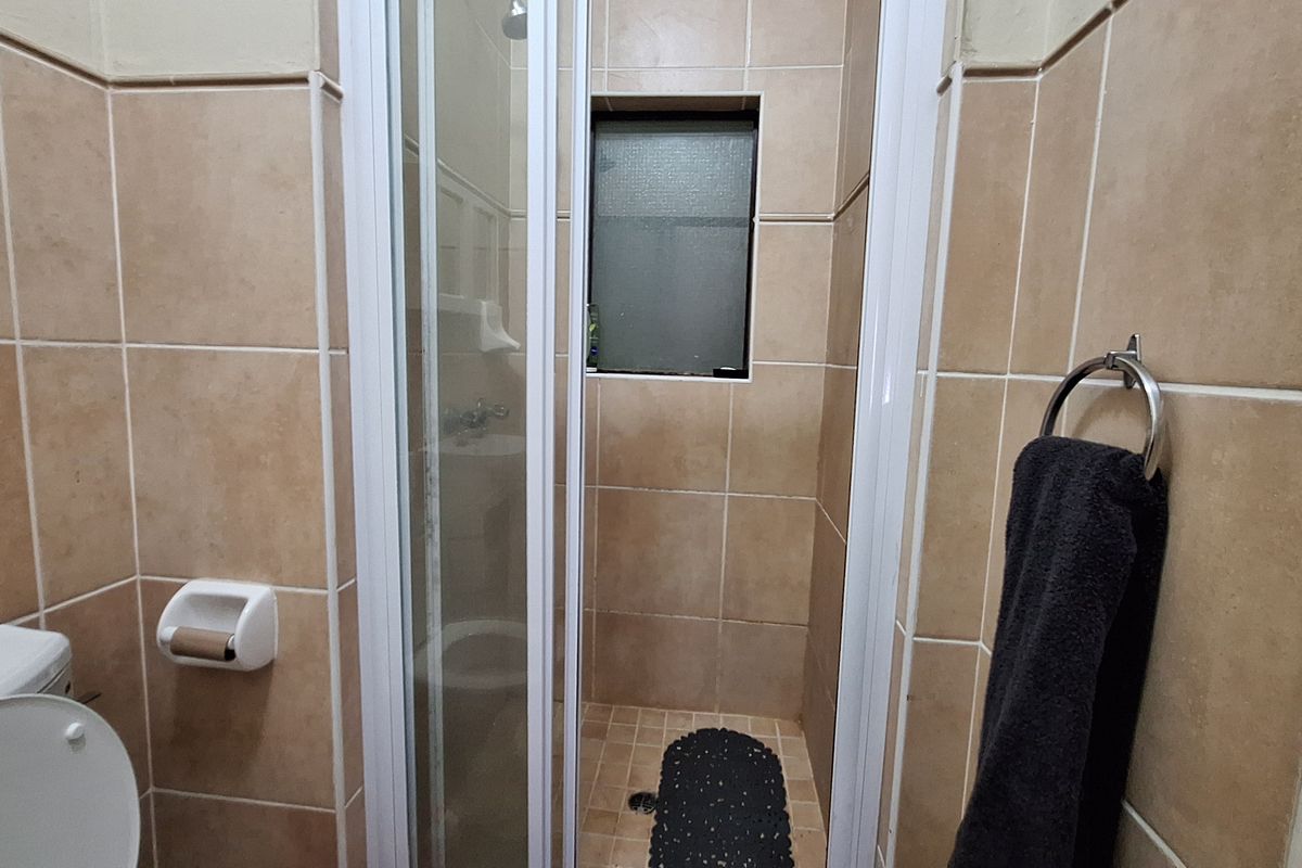A compact bathroom featuring a shower enclosure, toilet, and neutral wall tiling throughout.