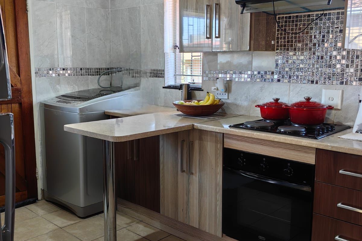 A functional kitchen featuring modern two-tone cabinetry, built-in oven and hob, tiled backsplash, and a convenient breakfast bar extension.
