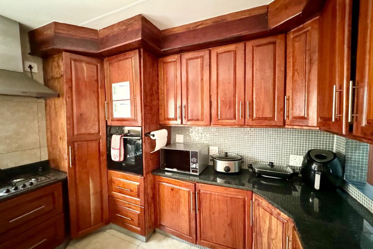 A functional kitchen featuring dark granite countertops, wooden cabinetry, a built-in oven, and a mosaic tile backsplash.