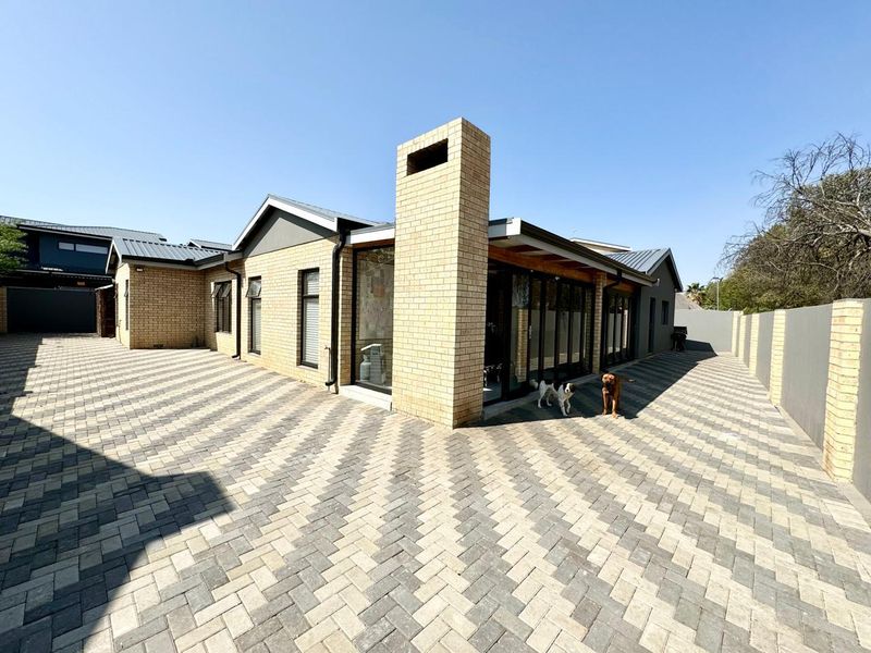 Rear view of a modern brick house featuring a prominent chimney, extensive paved courtyard, and large sliding glass doors leading to the interior.