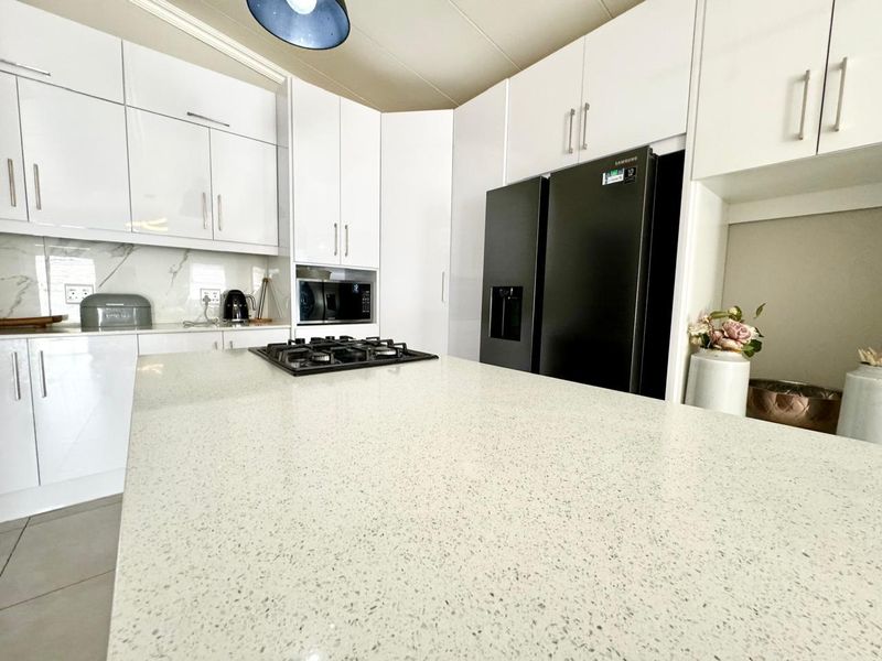 Modern kitchen featuring high-gloss white cabinetry, a spacious quartz island with an integrated gas hob, and a sleek marble-look splashback.
