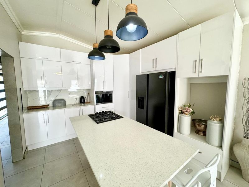 Modern kitchen featuring white gloss cabinetry, a stone island with a built-in gas hob, marble-look splashback, and contemporary pendant lighting.
