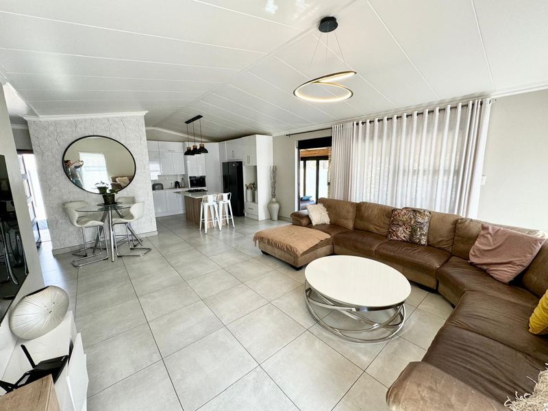 Spacious open-plan living area featuring large format floor tiles, a modern kitchen with island, and seamless flow to the outdoor patio area.