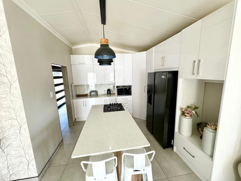 Modern kitchen featuring white high-gloss cabinetry, a central island with a gas hob, stone countertops, and tiled flooring.