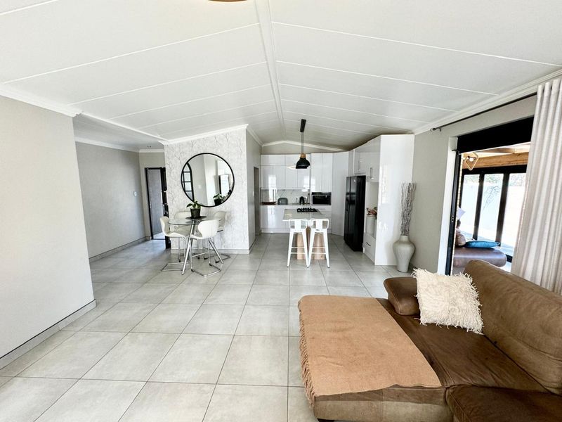 A bright open-plan living and kitchen area featuring large floor tiles, modern white cabinetry, a central kitchen island, and sliding doors leading to the patio.