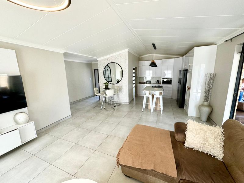 Modern open-plan living area featuring a sleek kitchen with built-in appliances, a central island, and neutral tiled flooring throughout.