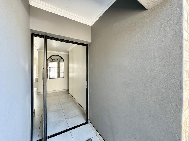 A bright and clean entrance area featuring tiled flooring, decorative cornicing, and a distinctive arched window, leading into the interior of the home.