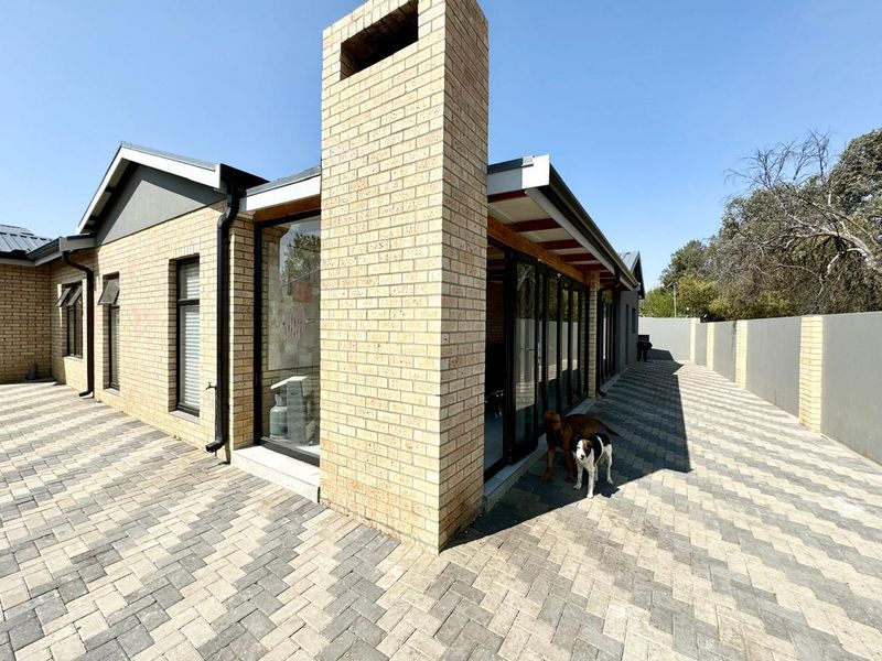 Rear exterior view of the house featuring a brick chimney, paved patio area, and modern sliding glass doors leading into the living space.