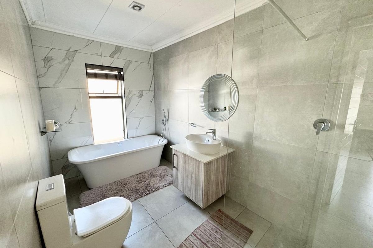 Modern bathroom featuring a freestanding bathtub, glass-enclosed shower, vessel sink vanity, and contemporary floor-to-ceiling marble-look tiling.