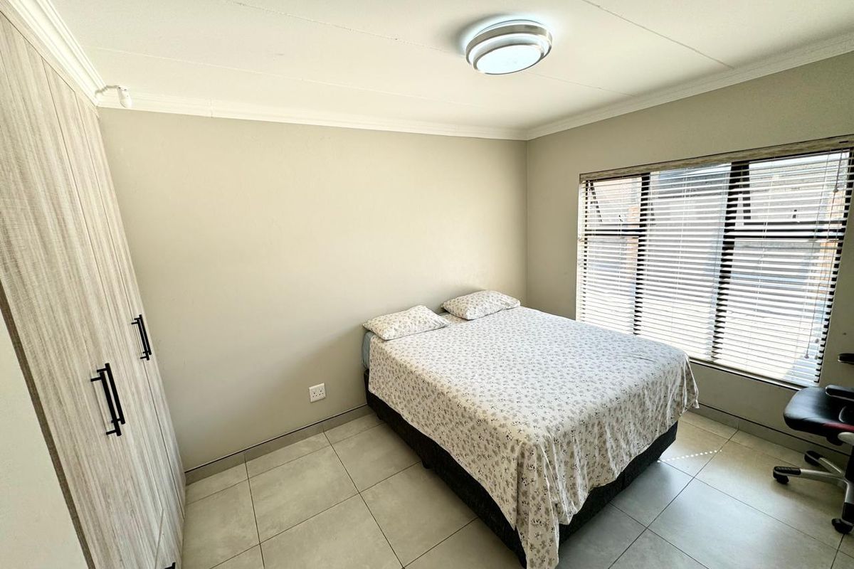 A well-maintained bedroom featuring neutral walls, tiled flooring, a built-in wardrobe, and venetian blinds for privacy.