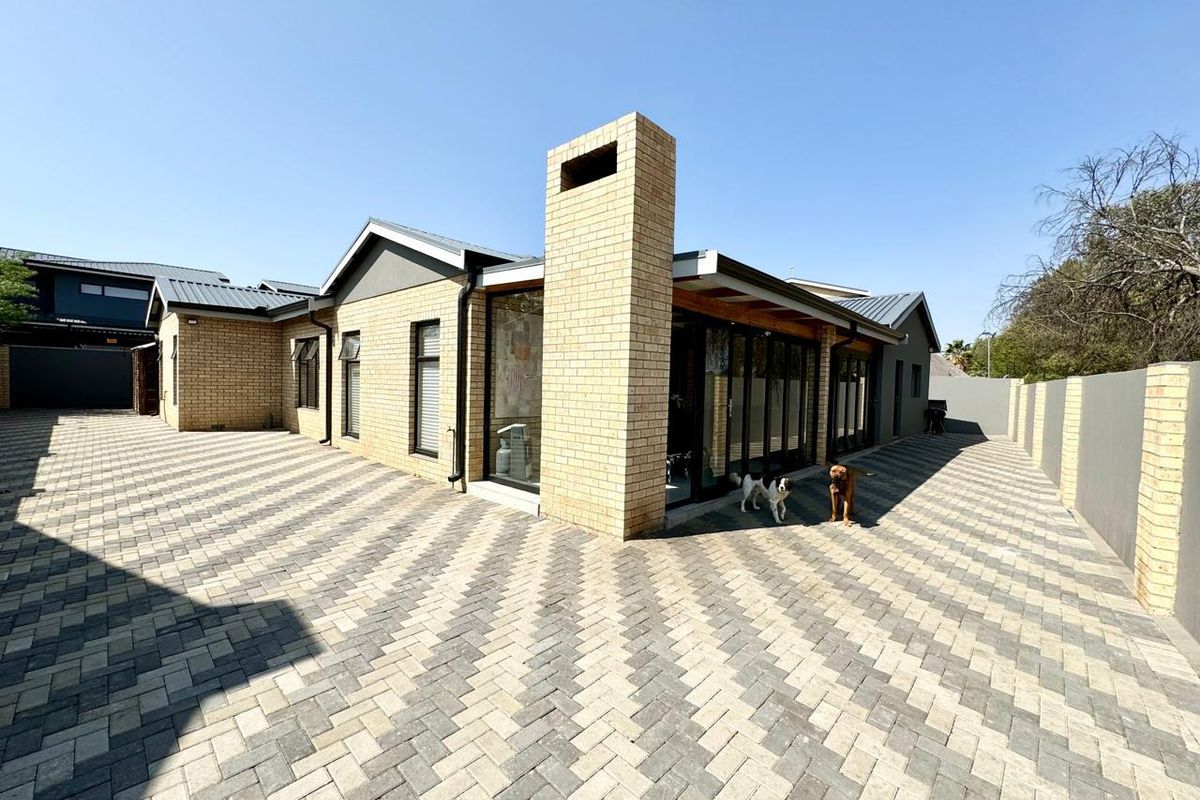 Rear view of a modern brick house featuring a prominent chimney, extensive paved courtyard, and large sliding glass doors leading to the interior.