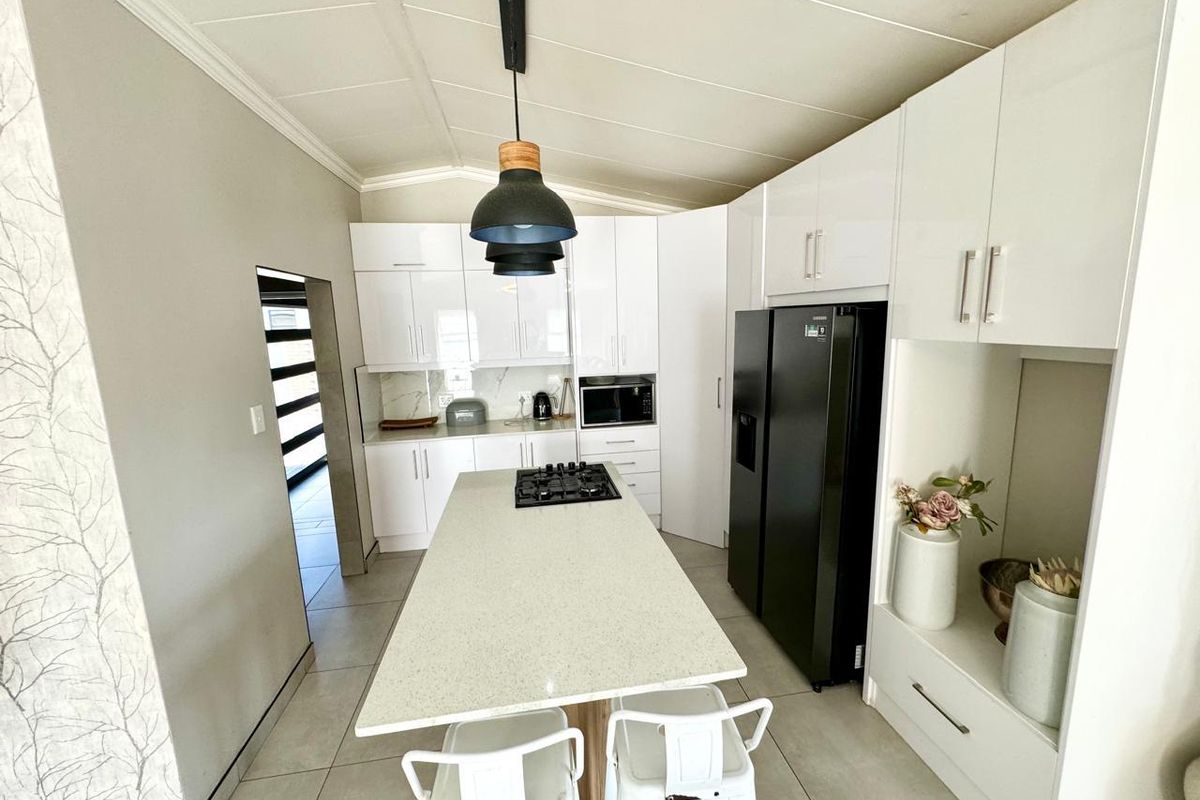 Modern kitchen featuring white high-gloss cabinetry, a central island with a gas hob, stone countertops, and tiled flooring.