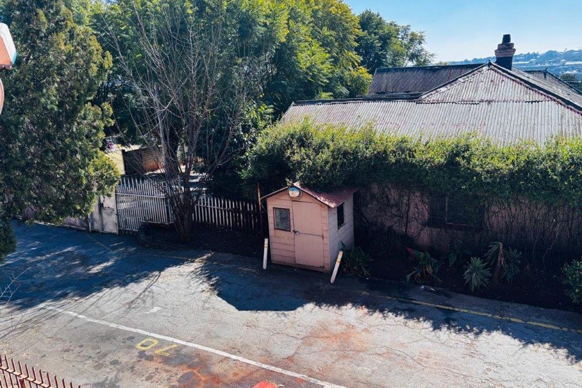 An elevated view of a property exterior featuring a weathered roof, paved driveway area, and a small detached utility structure.