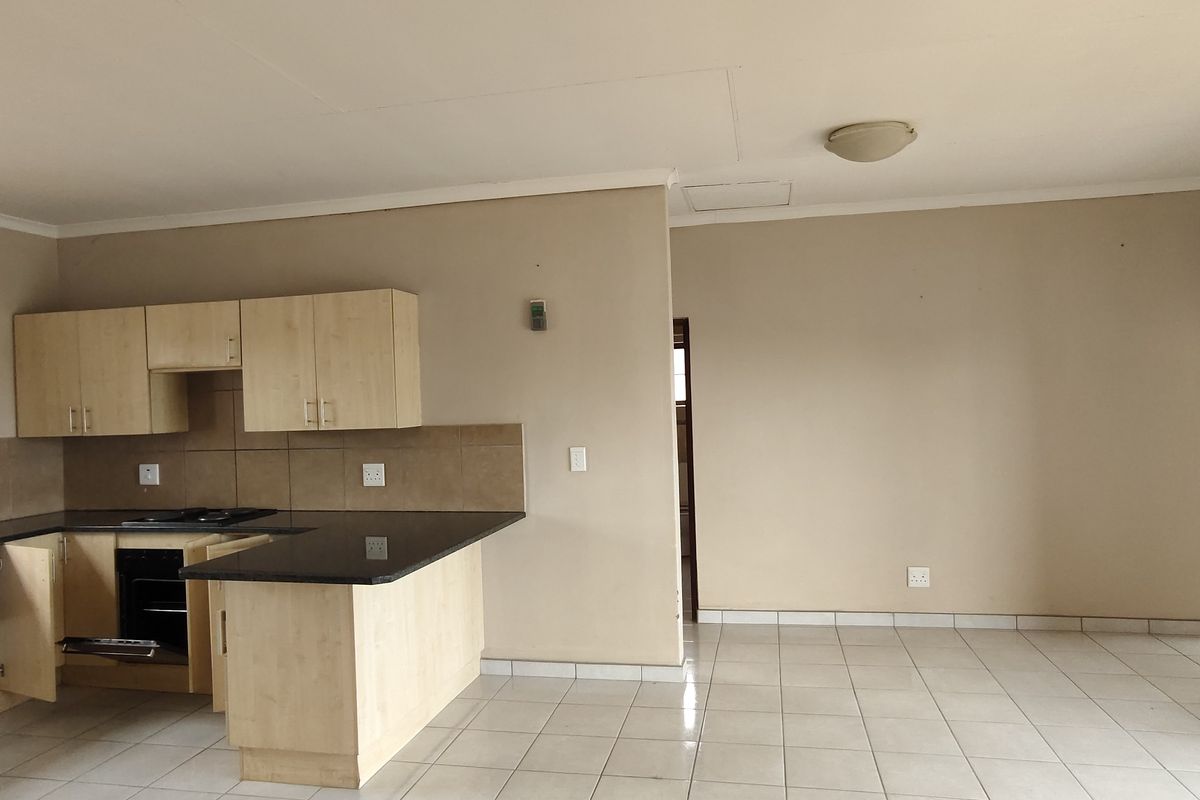 Open plan kitchen and living area featuring light wood cabinetry, granite countertops, built-in appliances, and neutral tiled flooring throughout.