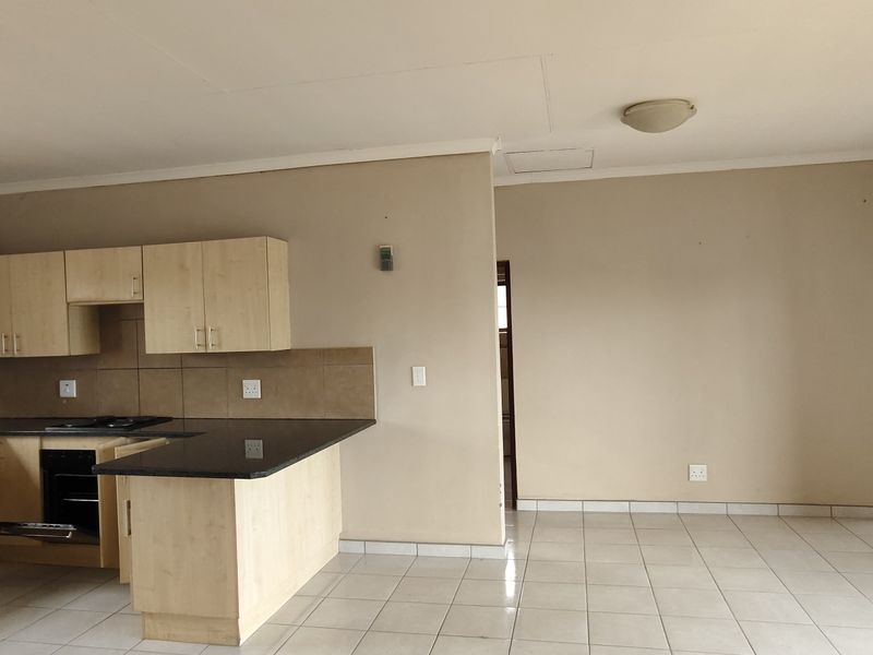 Open plan kitchen and living area featuring light wood cabinetry, granite countertops, built-in appliances, and neutral tiled flooring throughout.