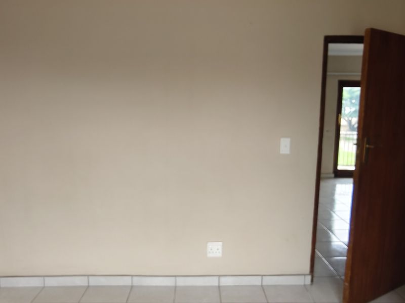 An empty bedroom featuring neutral wall paint, tiled flooring, and a wooden door leading to an adjacent space.
