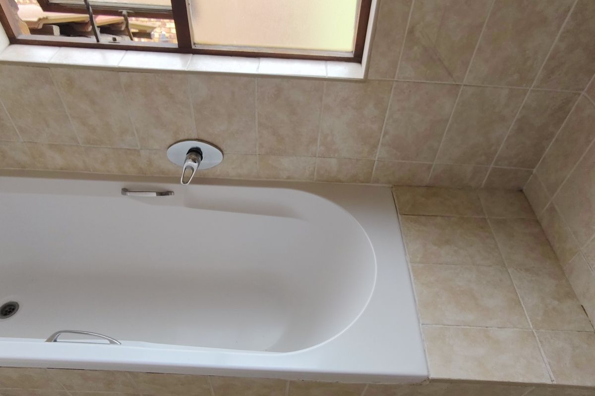 A functional bathroom featuring a built-in bathtub with wall-mounted mixer tap and neutral tiled surround.