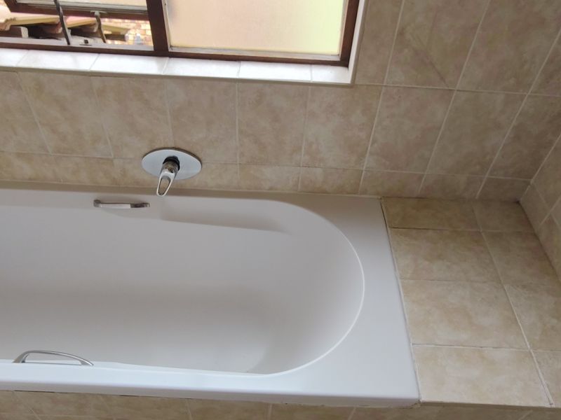 A functional bathroom featuring a built-in bathtub with wall-mounted mixer tap and neutral tiled surround.