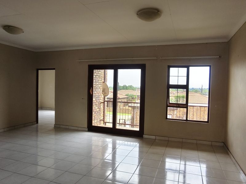 Spacious, empty living area featuring neutral tiled flooring, large sliding glass doors leading to a balcony, and ample natural light.