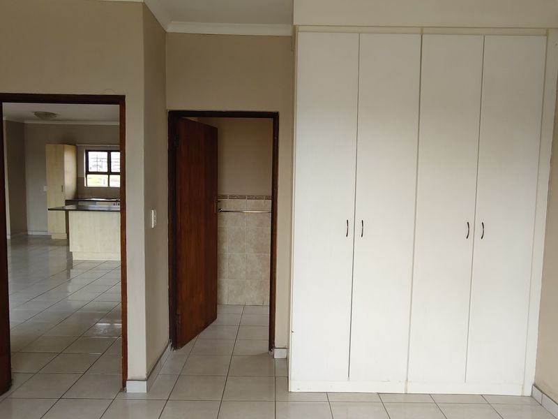 A spacious bedroom featuring neutral walls, tiled flooring, and ample built-in cupboard storage, with direct access to adjacent living and bathroom areas.