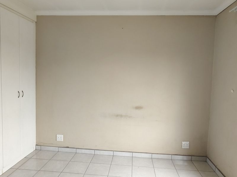 An empty bedroom featuring tiled flooring, built-in cupboards, and a window with security bars, requiring minor cosmetic attention to the walls.