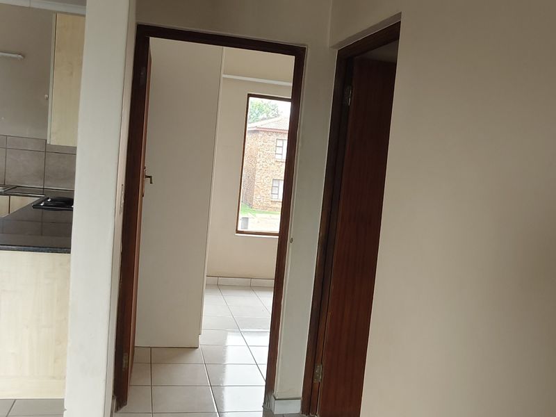 A neutral-toned hallway featuring tiled flooring and a ceiling access hatch, providing access to adjacent rooms within the apartment.