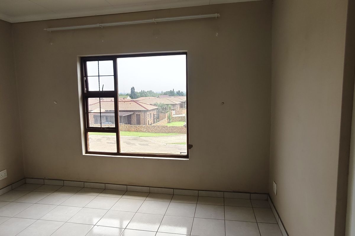 An empty bedroom featuring tiled flooring, neutral wall paint, and an aluminium window frame with a view of the surrounding residential area.