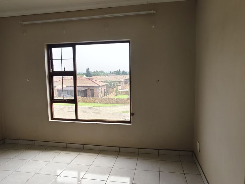 An empty bedroom featuring tiled flooring, neutral wall paint, and an aluminium window frame with a view of the surrounding residential area.
