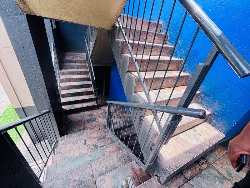 An outdoor stairwell featuring tiled steps and metal handrails, showing signs of wear and weathering on the surfaces and paintwork.