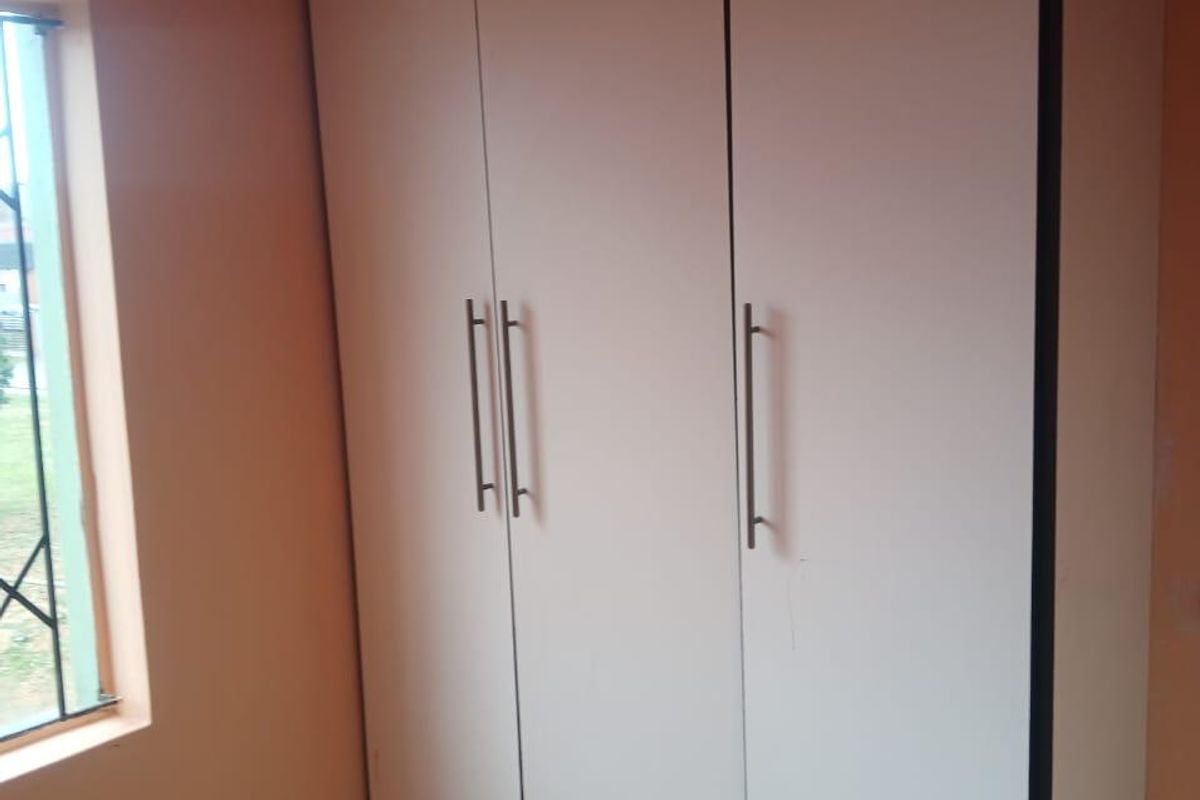A bedroom featuring a built-in wardrobe, tiled flooring, and a window, providing a functional space ready for personalization.