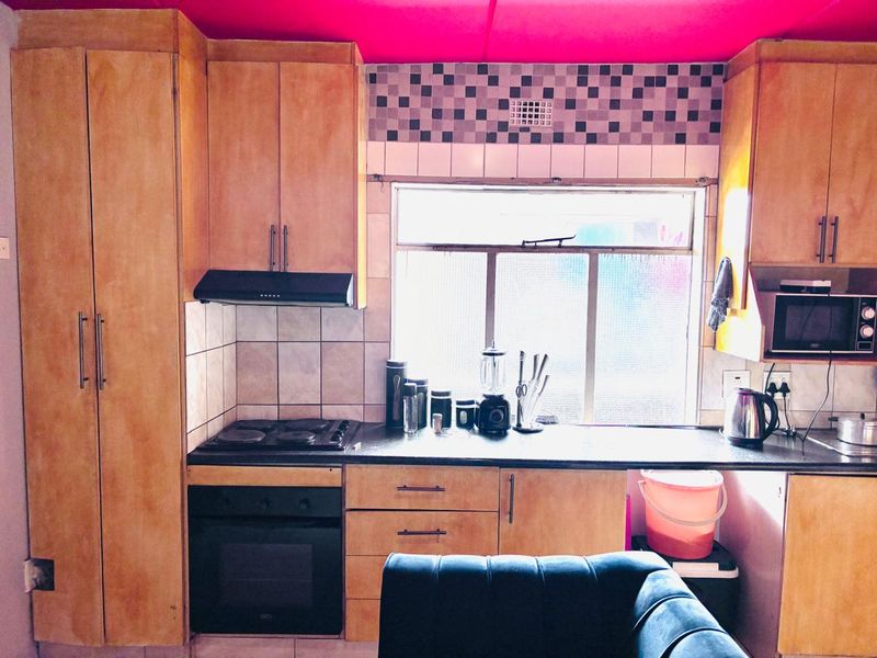 A compact kitchen featuring wooden cabinetry, a built-in oven and hob, and a tiled backsplash, requiring cosmetic updates to modernize the space.