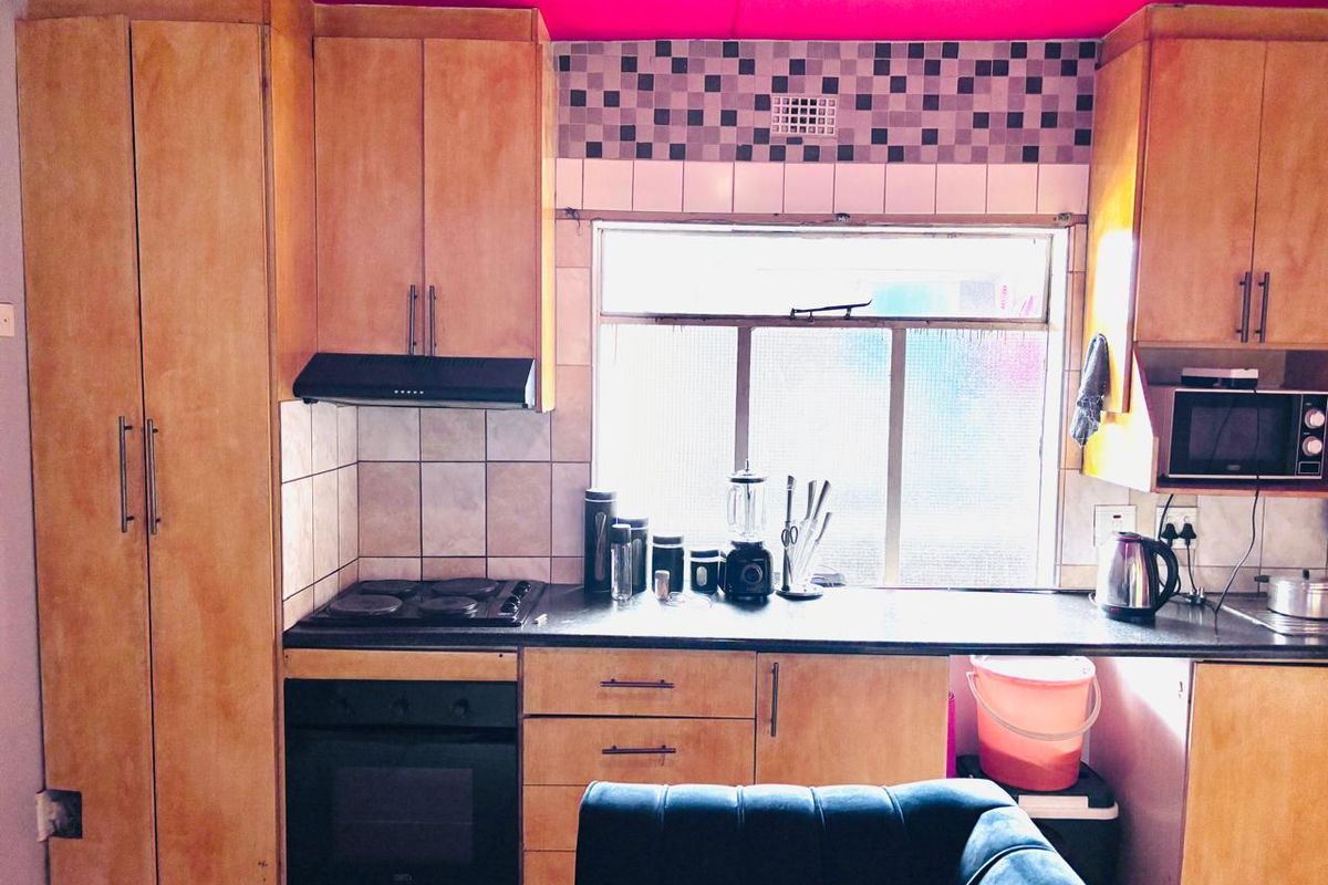 A compact kitchen featuring wooden cabinetry, a built-in oven and hob, and a tiled backsplash, requiring cosmetic updates to modernize the space.