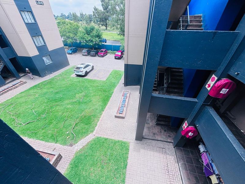 An elevated view of the apartment complex courtyard featuring a communal lawn, paved walkways, and external stairwell access.