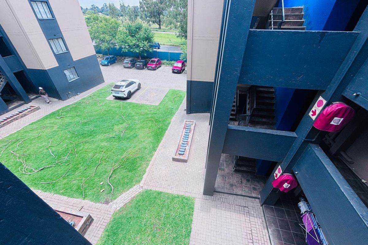 An elevated view of the apartment complex courtyard featuring a communal lawn, paved walkways, and external stairwell access.